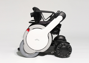 The WHILL is a modern black, white, and gray wheelchair with four wheels.